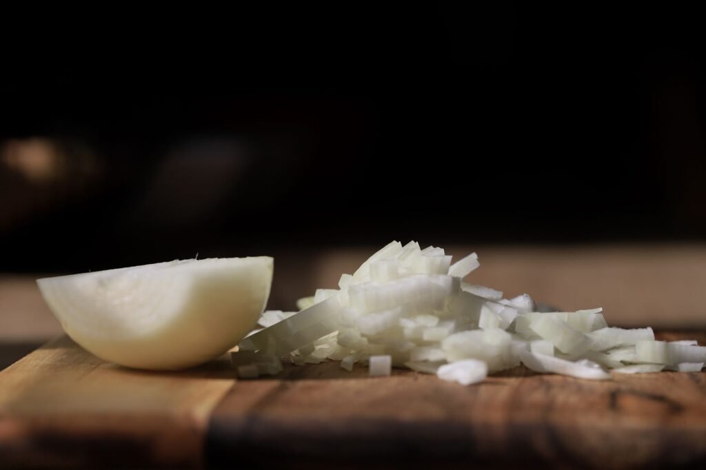 Diced white onion on a cutting board, showing why do onions make you cry once the cells are cut