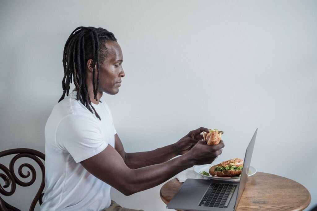Man eating a sandwich while working on a laptop, a distracted meal that feels less filling