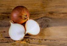 Whole and halved brown onion on a wooden table, the vegetable behind the question why do onions make you cry