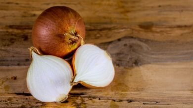 Whole and halved brown onion on a wooden table, the vegetable behind the question why do onions make you cry