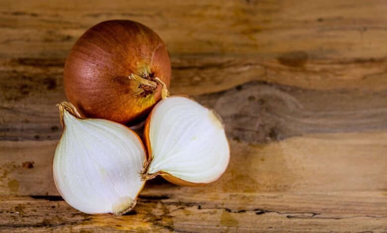 Whole and halved brown onion on a wooden table, the vegetable behind the question why do onions make you cry